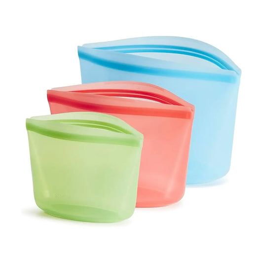 Three Stasher bags in different colors (e.g., blue, green, pink), arranged on a table.