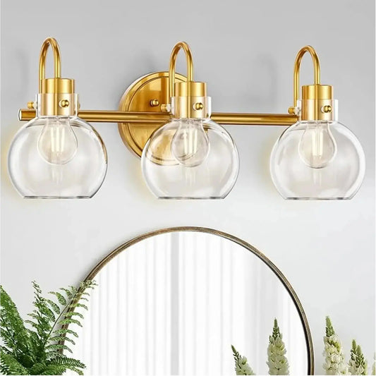 Full view of a 3-light brushed brass farmhouse vanity light fixture with globe clear glass shades.