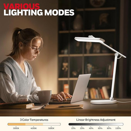 The adjustable arm of the Honeywell desk lamp positioned over a laptop and notebook.
