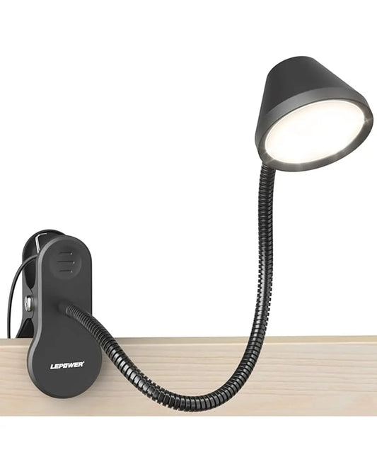 Black dimmable clip-on book light attached to a headboard, illuminating a paperback book.
