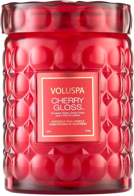 The Cherry Gloss candle glowing with a soft flame, casting a warm light in a cozy room setting.