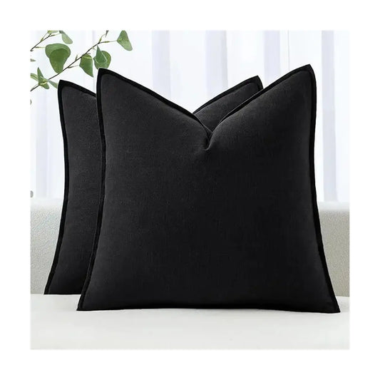 Full view of two black decorative linen throw pillow covers arranged on a neutral sofa.
